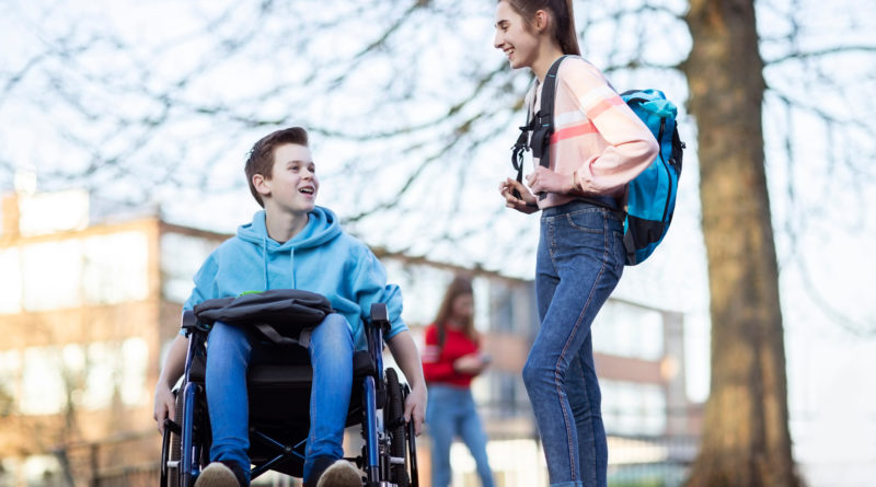 Schüler im Rollstuhl spricht mit Schülerin auf dem Schulhof.