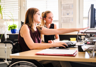 Zwei Frauen, eine davon im Rollstuhl, sitzen vor einem Computer und besprechen sich.