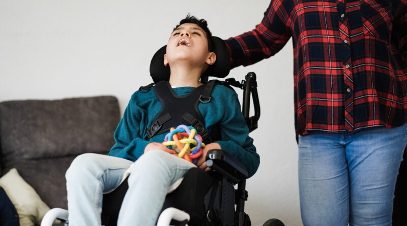 Pflegebedürftiger Junge sitzt im Rollstuhl mit Spielzeug.