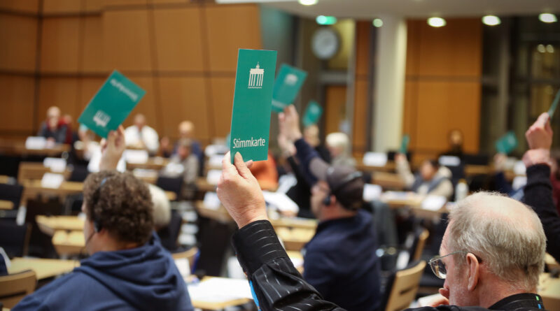 Teilnehmende im Abgeordnetenhaus heben grüne Stimmkarten hoch.