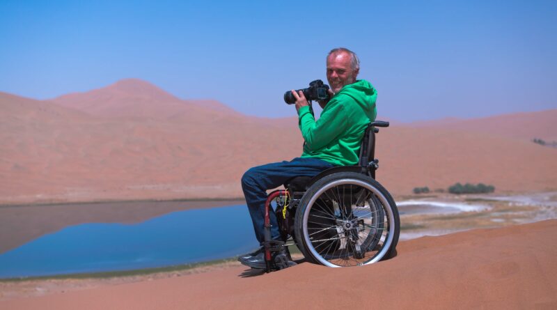 Andreas Pröve im Rollstuhl sitzt in einer Wüste und hält eine Kamera in den Händen.