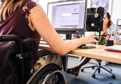 Rollstuhlfahrende am Schreibtisch mit einem Computer.