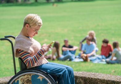 Frau sitzt im Rollstuhl und schaut auf ein Handy.