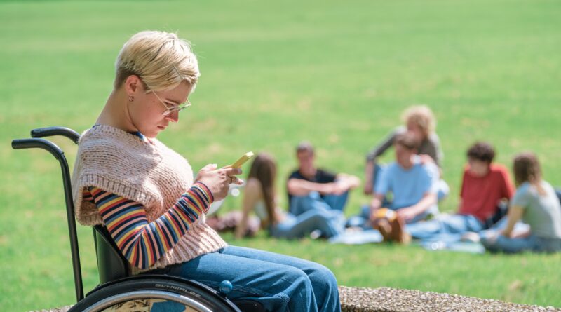 Frau sitzt im Rollstuhl und schaut auf ein Handy.