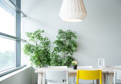 Ein Wohnzimmer mit einer grünen Pflanze, einer Lampe, einem weißem Tisch und drei weißen Stühlen und einem gelben Stuhl.