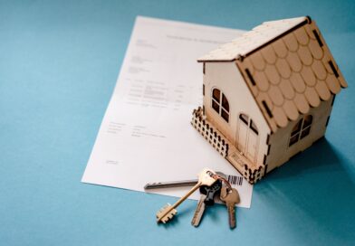 Modellhaus aus Pappe steht auf einem Blatt Papier. Davor liegt ein Schlüssel.